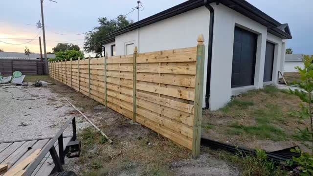 A long horizontal wood plank fence installed next to a white modern house.